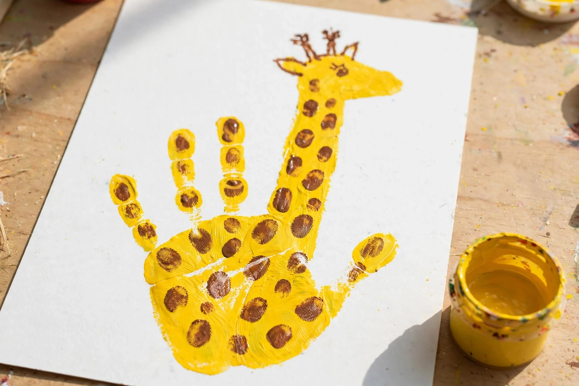 Yellow handprint giraffe craft with brown fingerprint spots and a long neck
